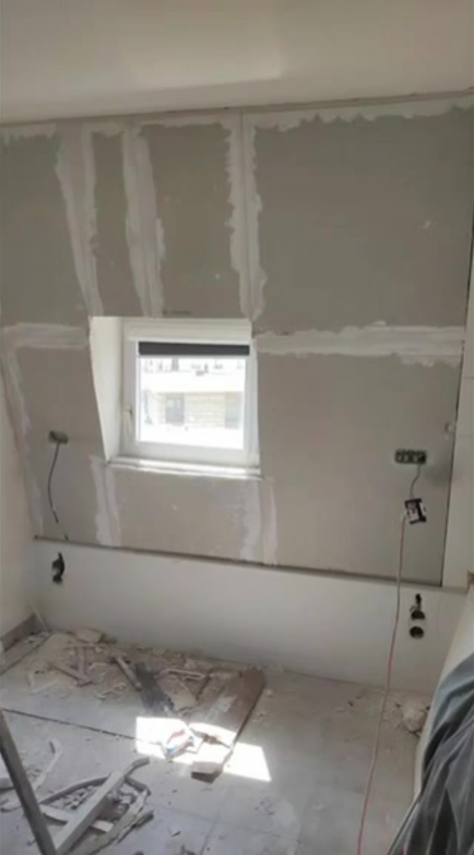 Rénovation intérieure d’un mur de façade en cours avec isolant et joints en placoplâtre autour d’une petite fenêtre, outils et câbles au sol. Ravalement paris obligation intégré.