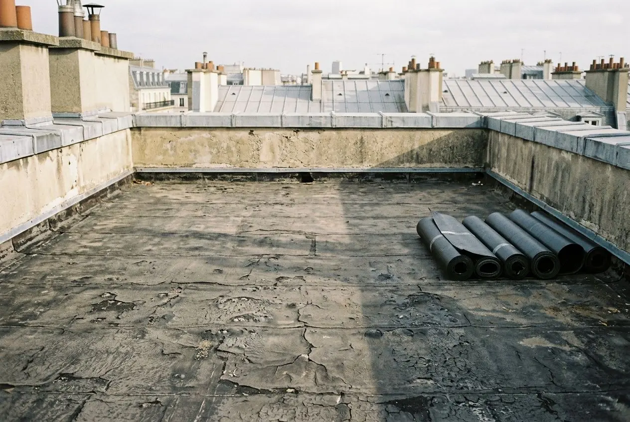 Toit plat en rénovation à Paris avec bâche et rouleaux de membrane d’étanchéité, surface asphaltée et joints visibles. Étanchéité toiture rénovation paris.