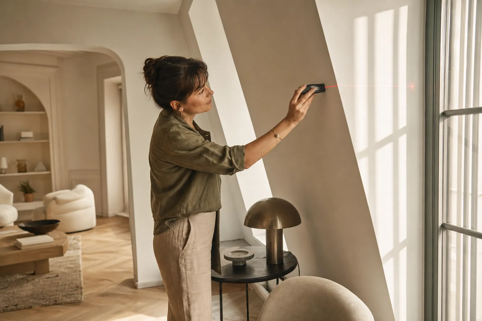 Consultante en agencement intérieur appartement paris utilisant un laser pour mesurer une façade intérieure lumineuse et moderne.